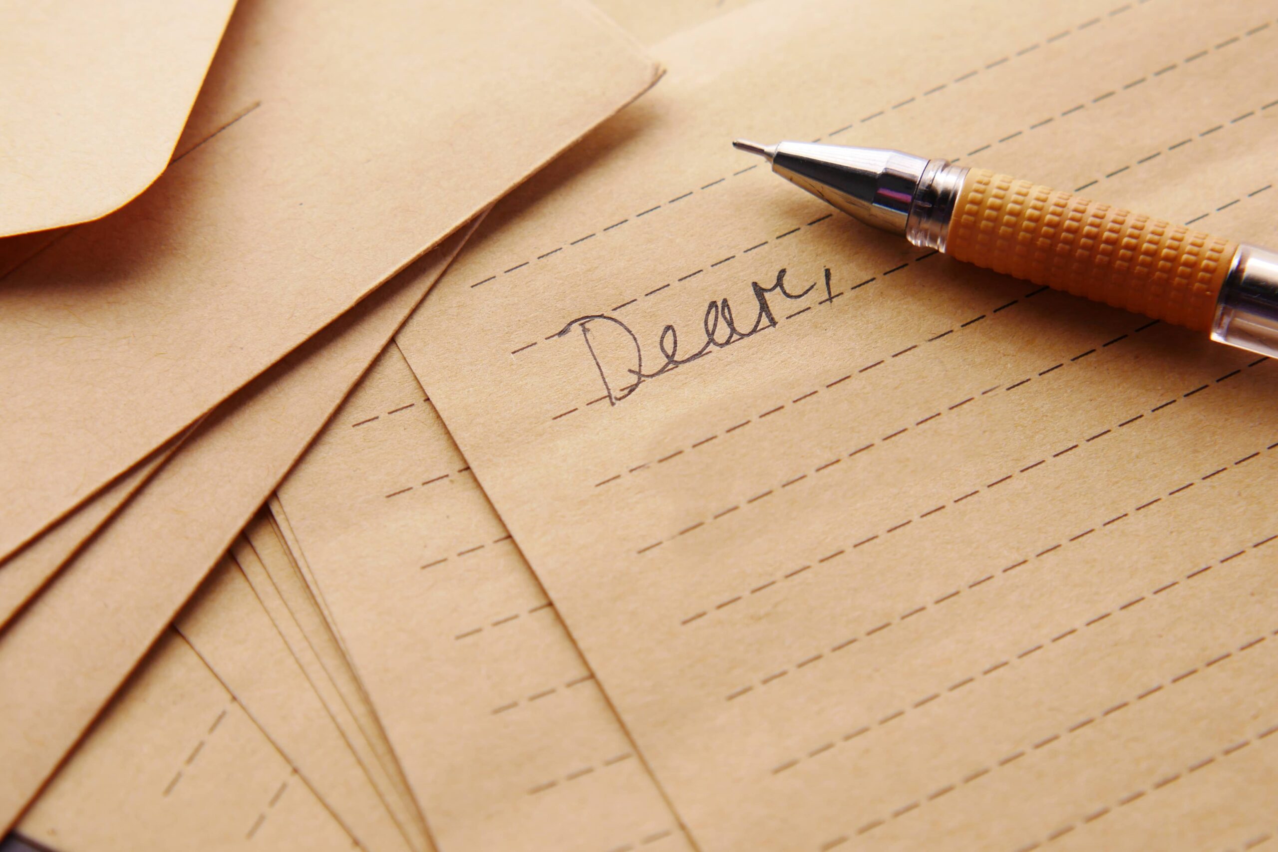 A lined piece of stationery with the word Dear in pen and the pen is resting on the paper.