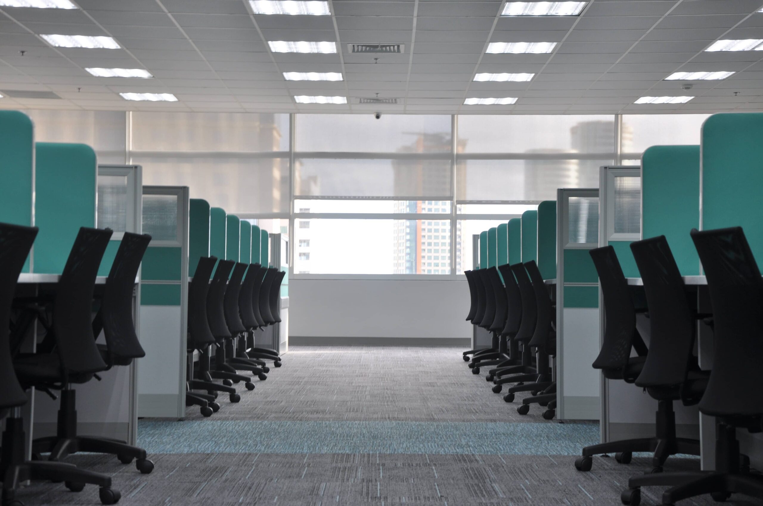 row of empty cubicles with black chairs and green cubicle walls