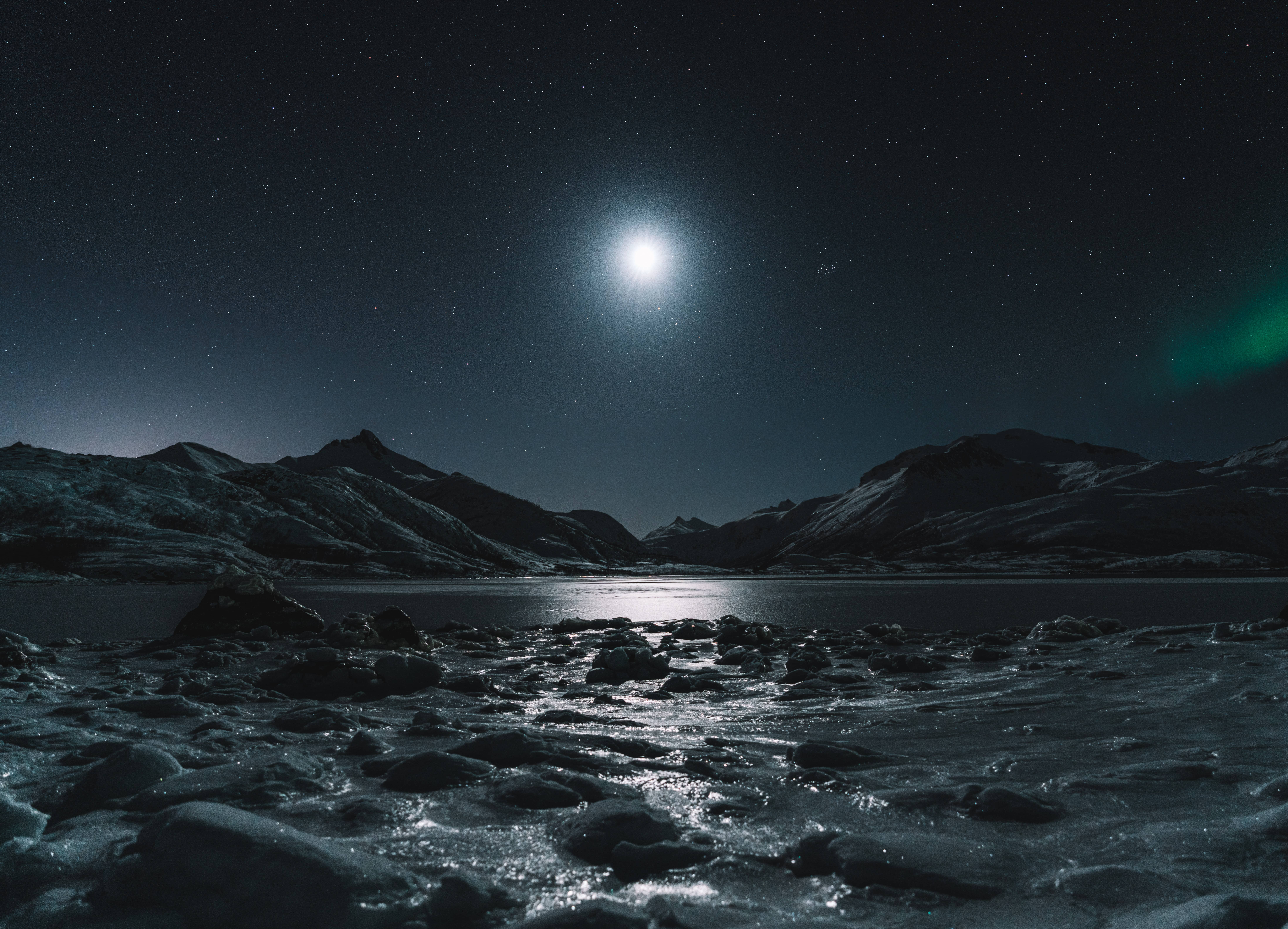 rocky shoreline with mountains in the distance, lit by a full moon in the center