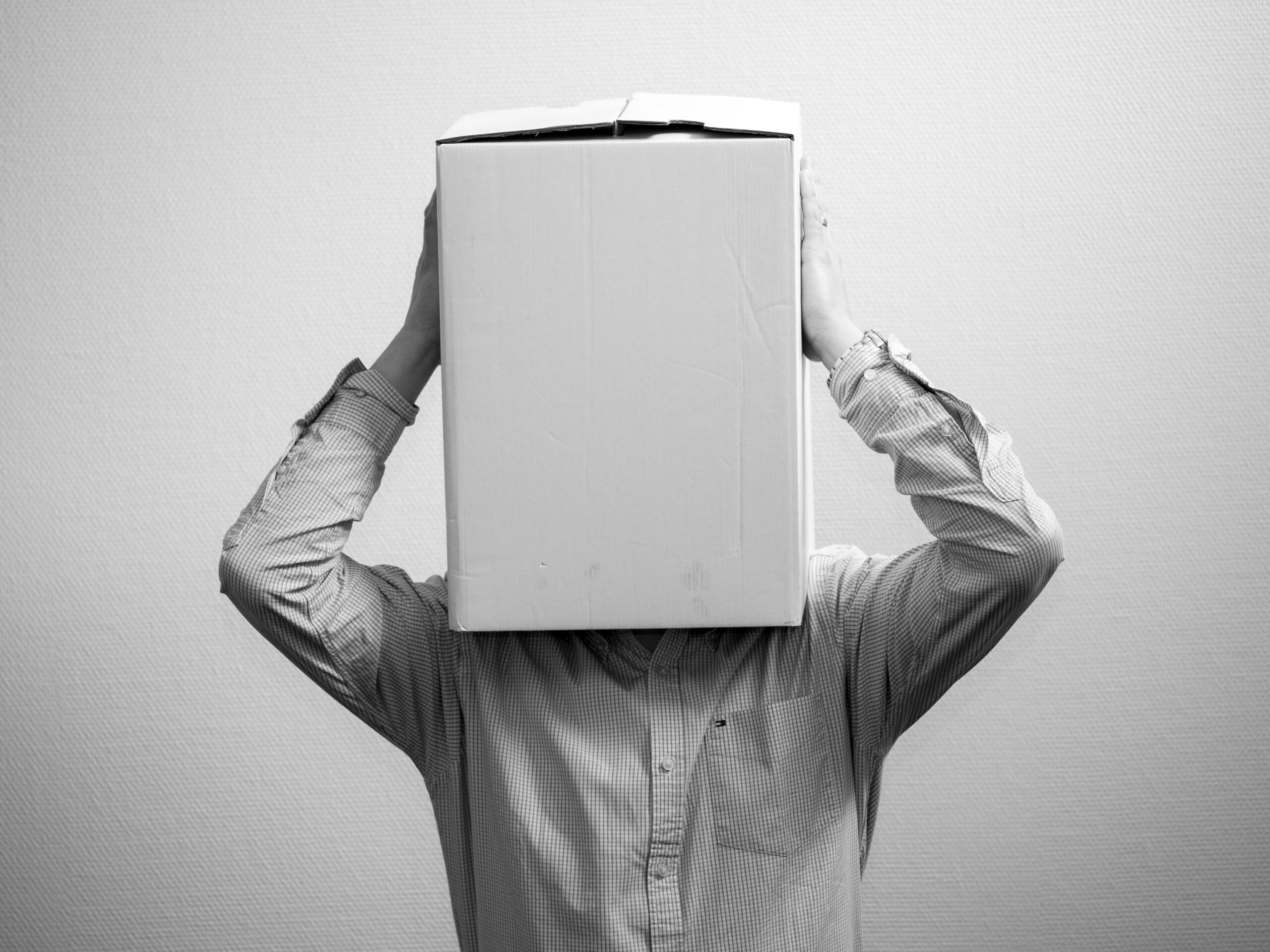 black and white image of a man standing with a brown box over his head
