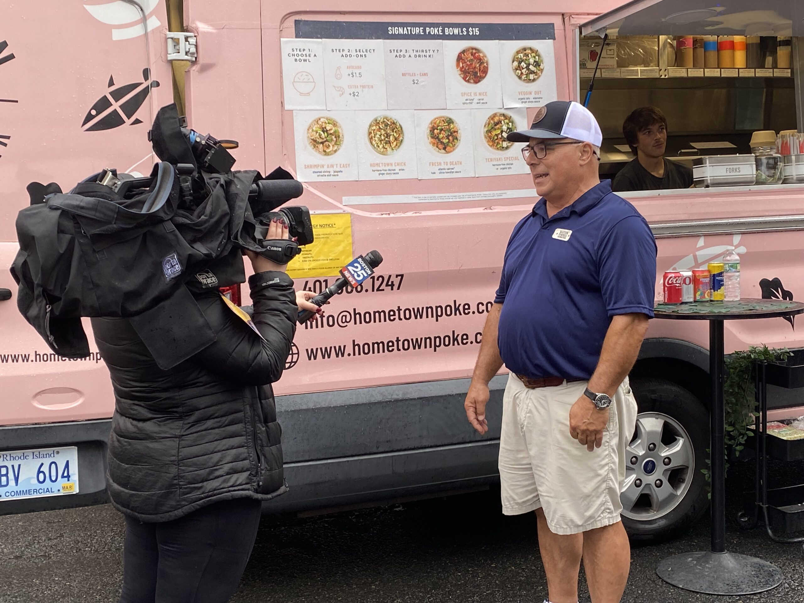 Man giving an interview in front of a news camera with a food truck as a backdrop