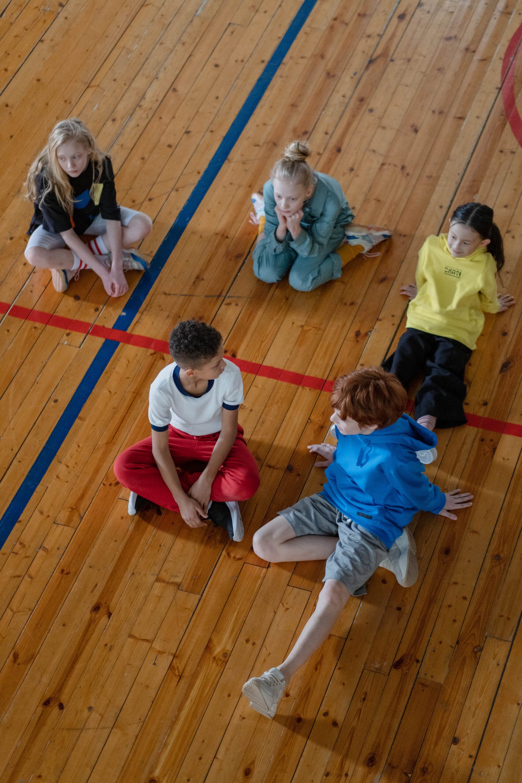 5 boys and girls sitting on a gymnasium floor